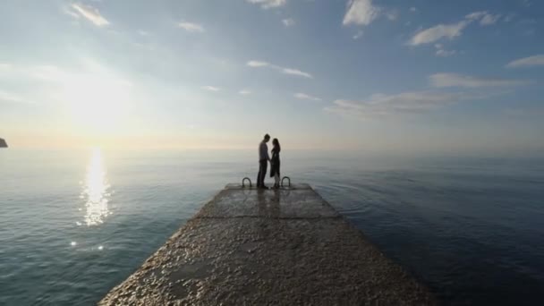 Любовники стоят на пирсе и держатся за руки на фоне моря . — стоковое видео