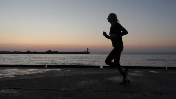 Dziewczyna sportowiec w godzinach wieczornych biegnie wzdłuż promenady. — Wideo stockowe