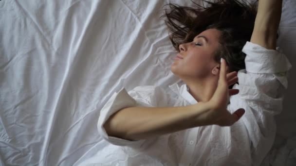 Młoda dziewczyna w białej koszuli tańczy w łóżku — Wideo stockowe