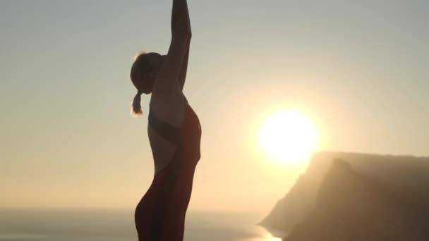 Woman doing yoga outdoors at sunset on a background of sea and mountains — Stock Video