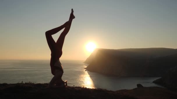 A menina pratica ioga na natureza contra o pano de fundo do mar e do pôr do sol . — Vídeo de Stock