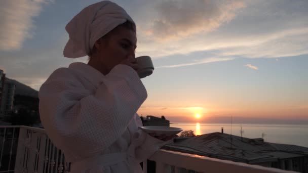 Kız kahve içiyor ve deniz ve akşam günbatımının güzelliğinin tadını çıkarıyor.. — Stok video