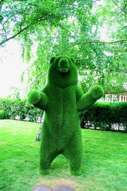 Yeşil bir parkın arka planındaki yeşil ağaçların dallarının altında plastik kürkten yapılmış bir ayı heykeli.