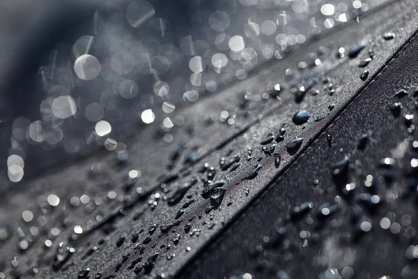 Streszczenie czarnego tła. Zamazane krople deszczu z bokeh na czarnym parasolu. Krople wody deszczowej na czarnej wodoodpornej tkaniny.Krople deszczu w słońcu. Tło z wolną przestrzenią. — Zdjęcie stockowe