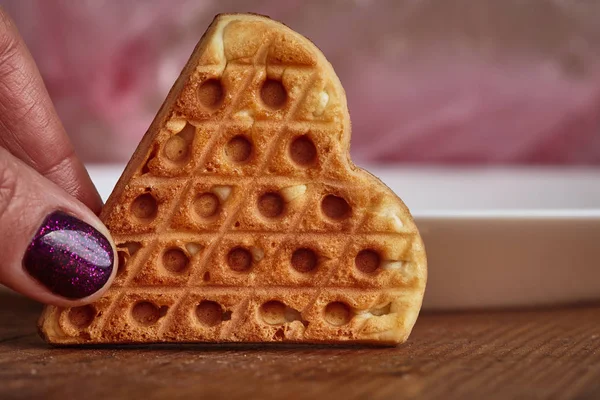 Galletas de azúcar en forma de corazón. La mano femenina sostiene la galleta en forma de corazón. Pasteles caseros. Una mujer sostiene galletas caseras en forma de corazón que yacen sobre la mesa . — Foto de Stock