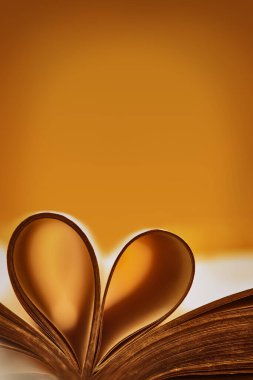 Bronz aksanlı soyut bir arka plan. Eski bir kitap. Katlanmış çarşaflardan katlanmış kalbi olan açık bir kitap. Eğitim kavramını seviyorum. Kitap sayfalarının arkaplanındaki bulanık kalpleri özetle.