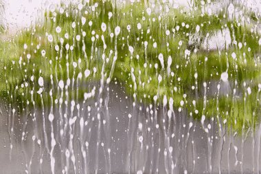 Soyut ıslak cam arka plan. Bulanık ağaç zeminli cam parçasına yağmur yağdır. Sisli bir pencereye yağmur damlaları. Sabun izleri ve lekeler içinde cam. Temizlik, temizlik, bahar