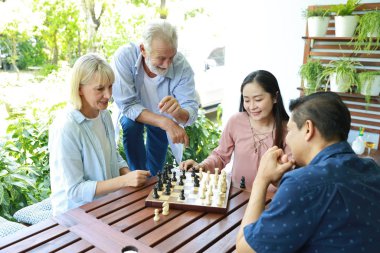 Bir grup çok ırklı son sınıf öğrencisi güneşli bir günde gülen yüzle satranç oynuyorlar. 