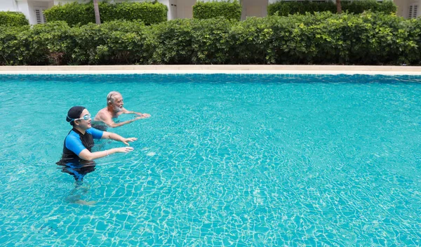 Vista lateral feliz anciano caucásico marido y anciano asiático esposa natación en piscina durante las vacaciones de jubilación con relajación en día soleado — Foto de Stock
