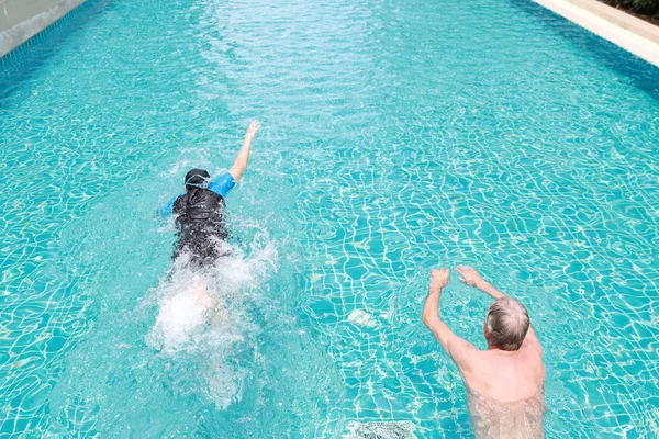 Vista de ángulo alto feliz anciano marido caucásico y anciano esposa asiática nadando en la piscina durante las vacaciones de jubilación con relajación en el día soleado — Foto de Stock