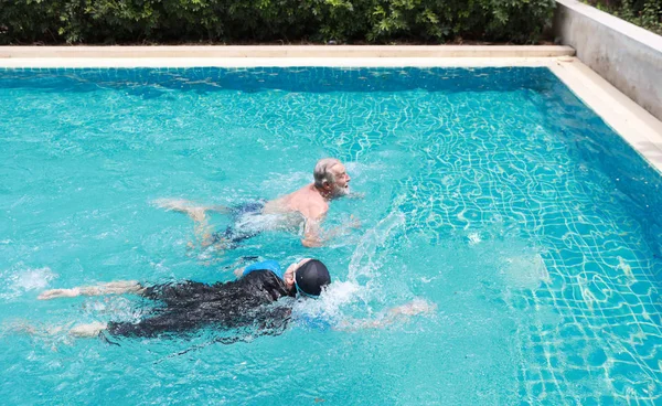 Vista lateral feliz anciano caucásico marido y anciano asiático esposa natación en piscina durante las vacaciones de jubilación con relajación en día soleado —  Fotos de Stock