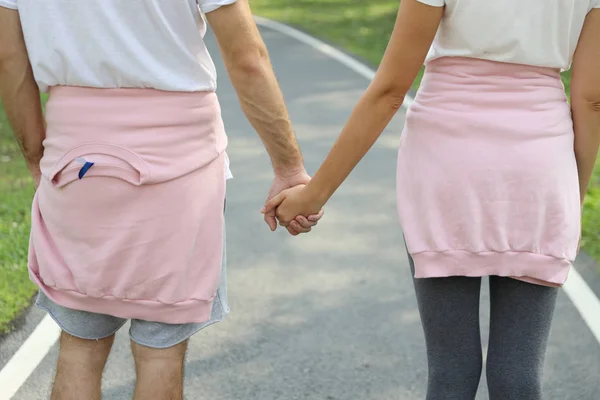 在夏天，穿着运动服手牵着手在公园里散步的年轻夫妇的后视镜和亲密接触（健康或友谊情人节的概念）) — 图库照片