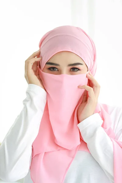 En ung arabisk kvinna i rosa hijab med självförtroende i studion. Isolerad vit bakgrund porträtt med vackra muslimska ögon flicka. Hon rör vid ansiktet. Reklamporträttkoncept. — Stockfoto