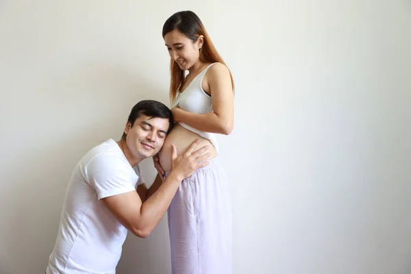 Schöner kaukasischer Ehemann hört seiner asiatischen schwangeren Bäuchlein-Frau zu, während er die Augen schließt mit glücklichem Lächeln Gesicht und Liebe — Stockfoto