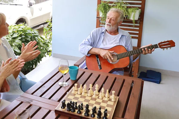 Egy csapat többnemzetiségű idős ember gitározik és énekel egy dalt, miután sakktáblán játszottak boldog mosolygós arccal a napsütéses napon. — Stock Fotó