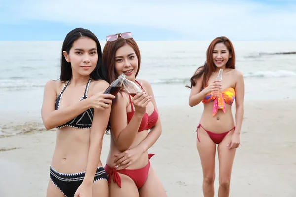 Sahilde bikini giyen bir grup mutlu Asyalı kadın. Bira şişeleri ve meşrubat şişeleri kızartıyorlar, birlikte eğleniyorlar ve eğleniyorlar. Gülümseyen güzel ve güzel vücutlu kızlar. — Stok fotoğraf
