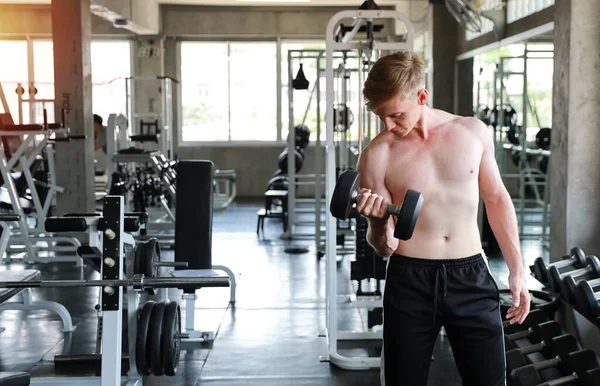 Mladý zdravý a sportovní pohledný běloch ve sportovním oblečení zvedající činku ve fitness tělocvičně. Koncept cvičení — Stock fotografie