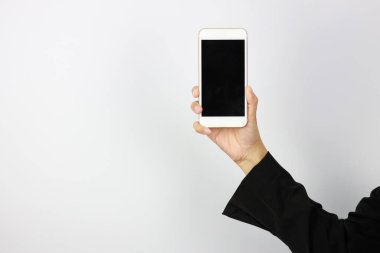 İş kadını, siyah takım elbiseli üniformalı, siyah ekranlı cep telefonunu beyaz arka plan stüdyosunda tutuyor ve gösteriyor.)
