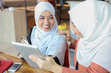 Genç Müslüman iş kadınları kredi kartı, cep telefonu ve gülen yüzlü tablet kullanarak tartışıyor, alışveriş yapıyor ve online ödeme yapıyorlar.