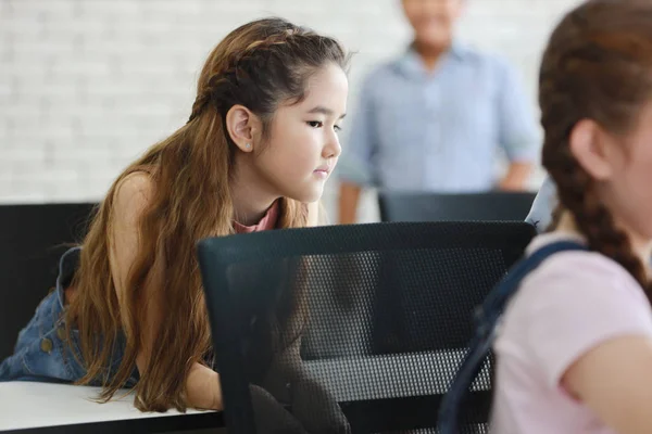 Şirin ve zeki küçük kız bir şeye ya da birine bakarken günlük kıyafetiyle sınıfta oturuyor ve ders çalışıyor.