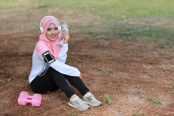 漂亮的健美运动员亚洲穆斯林女子运动后喝水 年轻可爱的女孩穿着运动服 戴着哑铃 在户外运动后用耳机休息 体育概念 — 图库照片