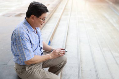 Asyalı gezgin elleri mavi gömlekli şehir merkezinde merdivenlerde oturuyor ve cep telefonu kullanıyor. 