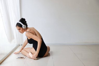 Siyahi spor giyimli, kulaklıklı çekici Asyalı kadın. Cep telefonundan müzik dinleyen güzel kız bale eğitimi alırken (teknoloji ve sağlıklı konsept)