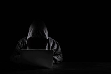 Siyah başlıklı tehlikeli bir hacker bilgisayar kullanıyor, güvenlik veri sunucusuna giriyor. Oturuyor, siyah arka plan üzerinde çalışıyor. İnternet suçları, siber saldırı güvenlik kavramı