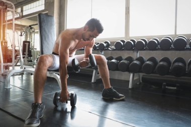 Bıyıklı yakışıklı beyaz adam gülümseyen yüzüyle spor salonunda halteri kaldırıyor.