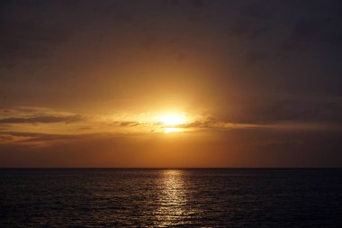 Denizde harika bir gün batımı. Güneş ufukta küçük bulutlar içinde batar. Deniz kıyısında harika bir yaz tatili akşamı..