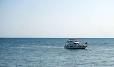 Deniz ve ufukta kırmızı bayraklı beyaz bir motorlu tekne. Yat üstünde harika bir deniz yolculuğu. Denizde unutulmaz bir yaz tatili.                     