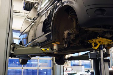 Benzin istasyonundaki bir araba tamir için kaldırılır. Arabanın ön tekerleği sökülmüş, ön süspansiyonun unsurları görünür durumda. Bir benzin istasyonunda konsept servis ve araba tamiri.