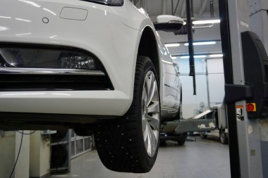 Benzin istasyonunda beyaz lüks bir araba bakım ve onarım için kaldırılır. Ön tampon, tekerlek, sis lambası, arka planda servisin iç kısmı bulanık. Kavram.