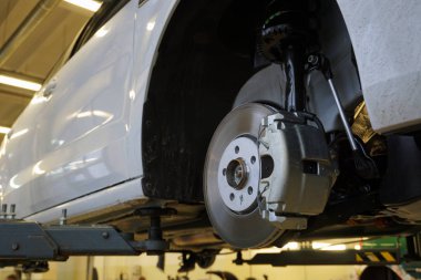 A modern luxury car at a service station is lifted on a lift for repair. Front brake disc, caliper. Quality after-sales service concept.