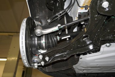 Elements and design of the front suspension of a modern car. Drive shaft with protective cover, suspension arm, steering rod and steering tip, wheel bearing housing, brake tubes and hoses.