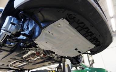 White luxury car raised on a lift in service. An additional crankcase protection is installed on the vehicle. Additional equipment and car tuning concept.