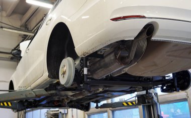 White luxury car raised on a lift in service. All wheels removed on the car. Visible rear suspension elements, rear beam, springs, rear muffler. The concept of quality car service.