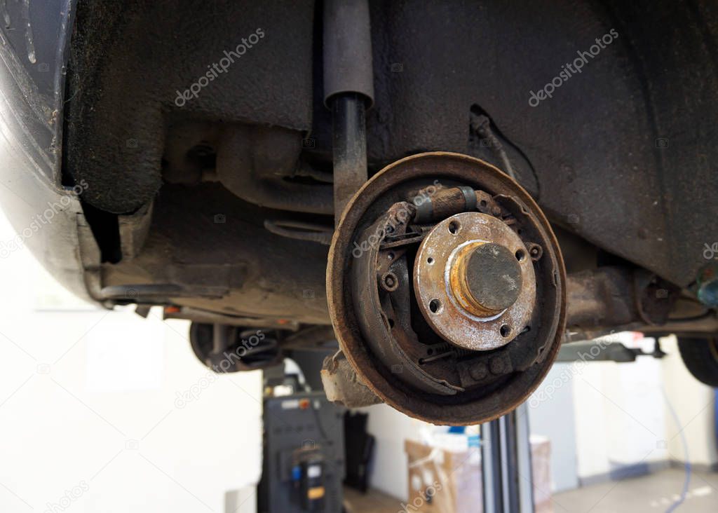 Old worn rusted rear brake of a car. The car is lifted on a lift in service to repair or replace the brake mechanism. Serviceable brakes mean road safety.