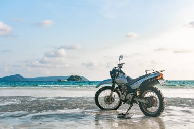 Kumsalda gümüş bir motosiklet duruyor.