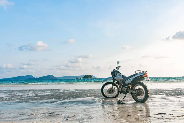 Kumsalda gümüş bir motosiklet duruyor.