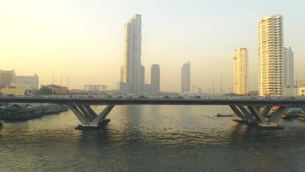 Drone shot flying along Chao Phraya River over Taksin Bridge, towards Bangkok skyscrapers — ストック動画