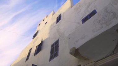 Essaouira, Fas 'ta mavi pencereli uzun beyaz bir bina boyunca el kamerasıyla çekilmiş.