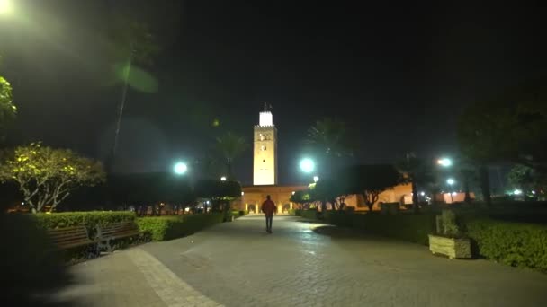 Disparo de mano que sigue a una persona que camina hacia la mezquita de Koutoubia por la noche — Vídeos de Stock