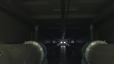 Işıklar uzun bir koridoru aydınlatıyor. Büyük borular akıyor.