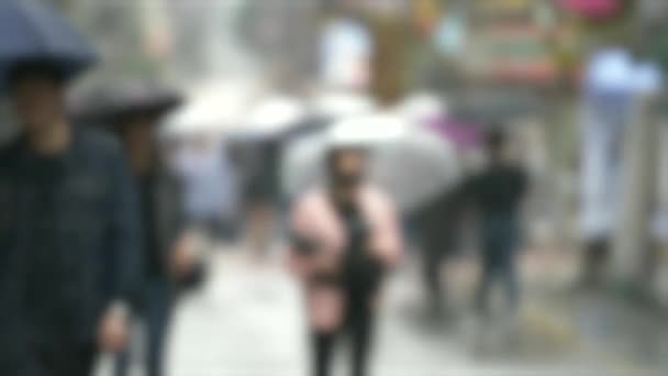 An out of focus shot of people walking down a wet street with umbrellas in South Korea — Stock Video