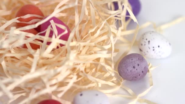 Colpo ravvicinato di uova di cioccolato colorate e sparse intorno a un nido di paglia rotante — Video Stock