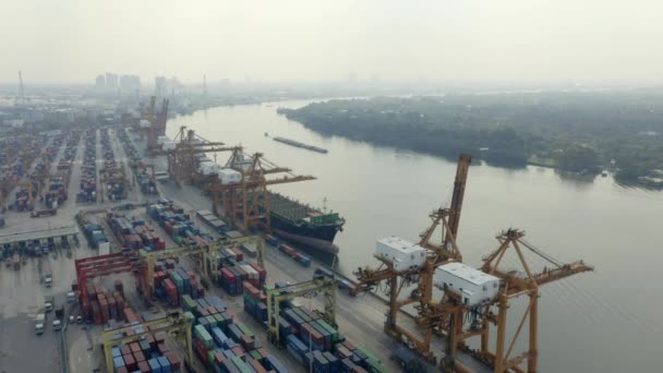 Aerial view of a shipping container port opposite a wooded riverbank with Bangkok in the background — Stock Video