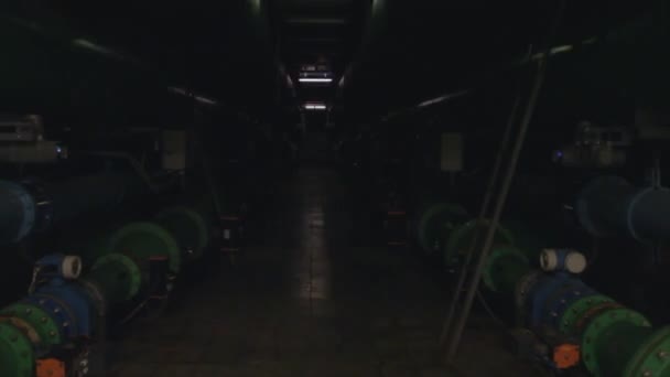 El seguimiento a través de un pasillo industrial con tuberías de agua y escaleras en las luces vienen — Vídeo de stock