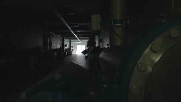 Tracking across an industrial corridor with pipes and valves as the lights come on — Stock Video