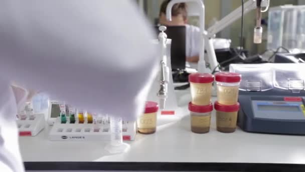 Tracking past a scientist at a laboratory bench with colorful test tubes and samples — Stock Video